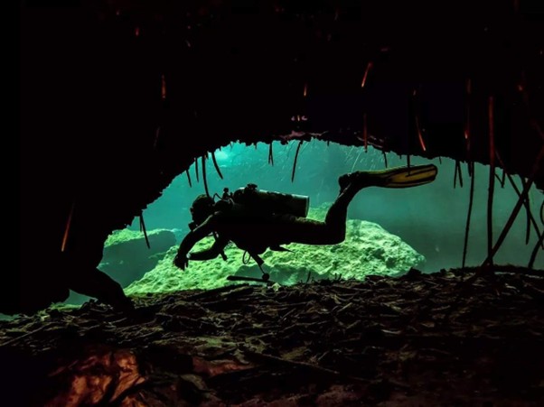 Buceador técnico explorando una cueva sumergida con configuración de montaje (backmount) y linternas de alta potencia.